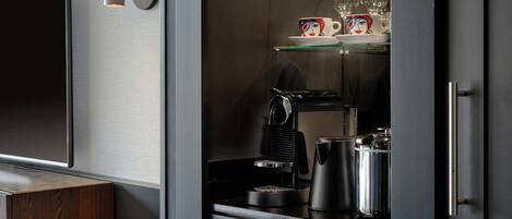 Une petite cuisine équipée comprenant une machine à café, une bouilloire et de la verrerie, le tout rangé sur une étagère.