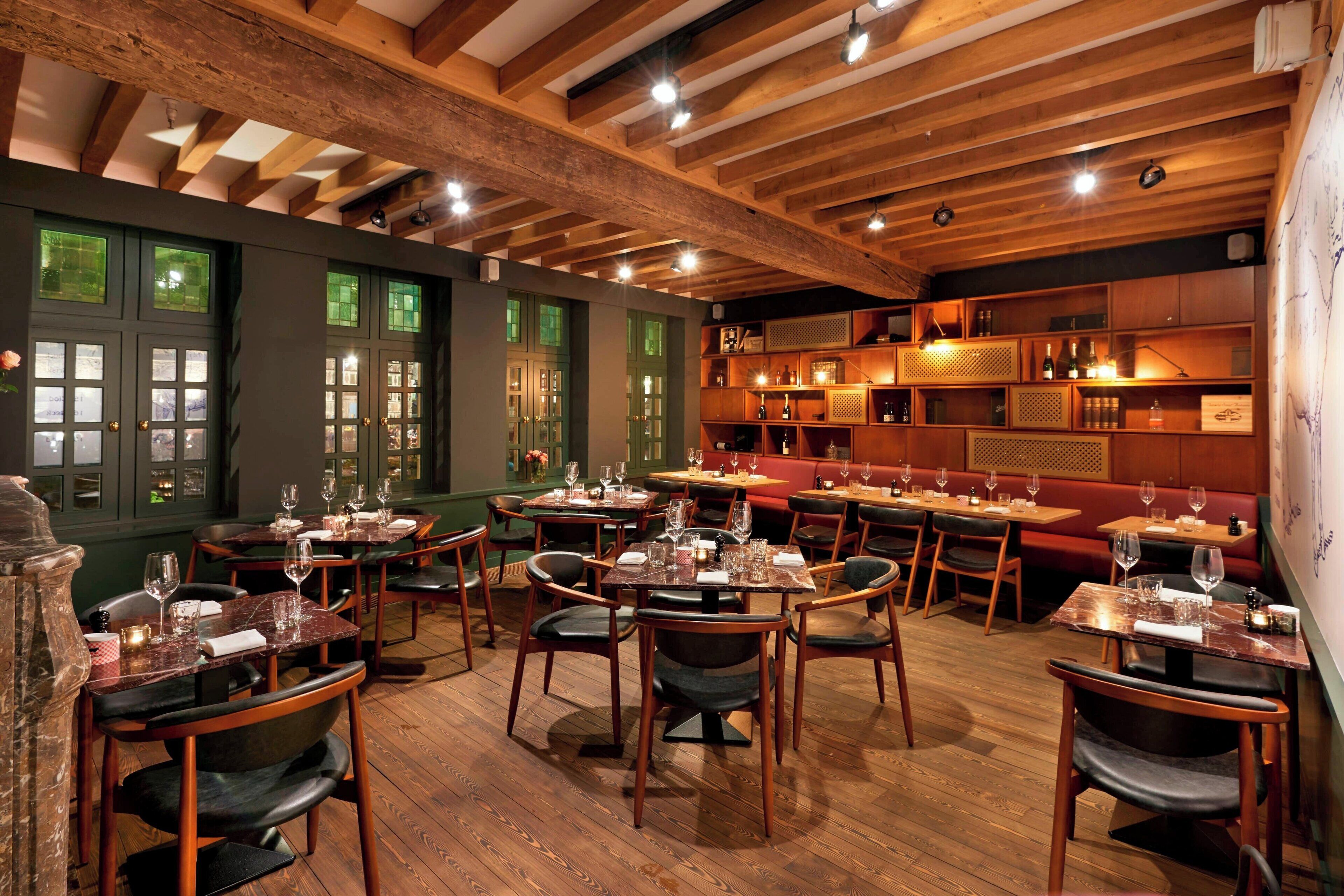 Un restaurant avec des poutres en bois, des murs verts et de nombreuses tables à manger entourées de chaises.