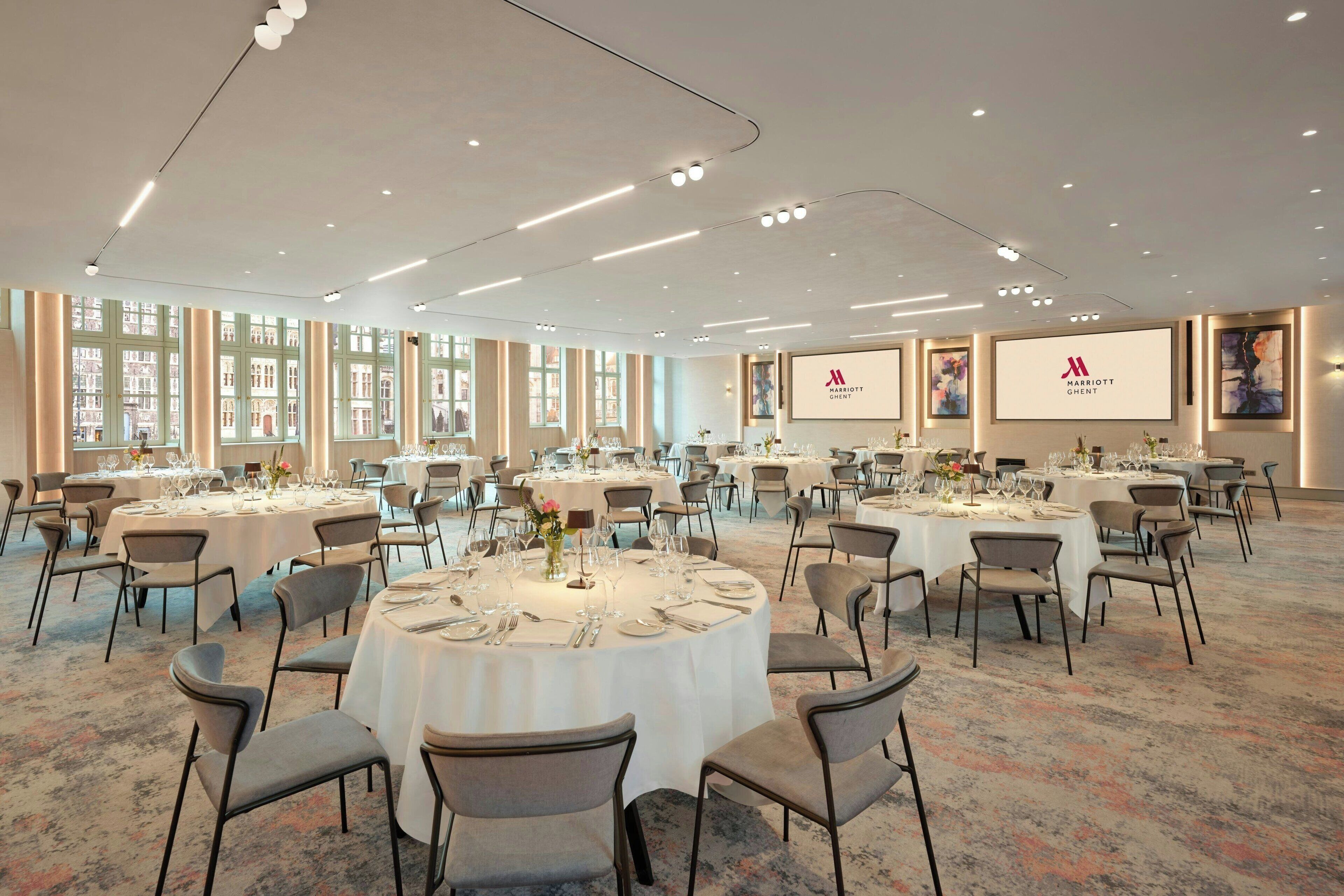 Une grande salle de conférence dotée de plusieurs tables rondes, chacune recouverte d’une nappe blanche et agrémentée de chaises et de verres.