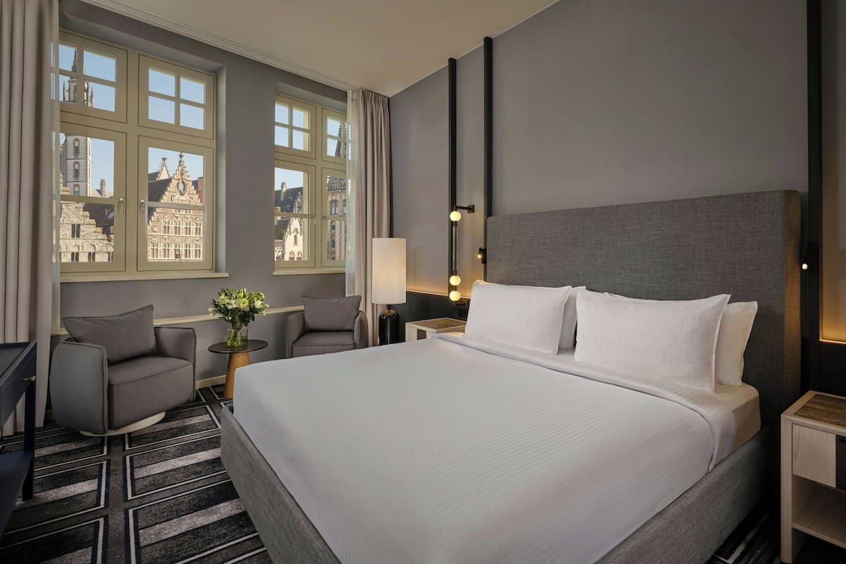 Una habitación de hotel con una cama grande, un escritorio, una silla y vistas a un paisaje urbano a través de la ventana.