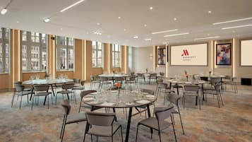Een conferentiezaal van een Marriott hotel met meerdere ronde tafels, stoelen en een groot scherm waarop het Marriott logo staat.