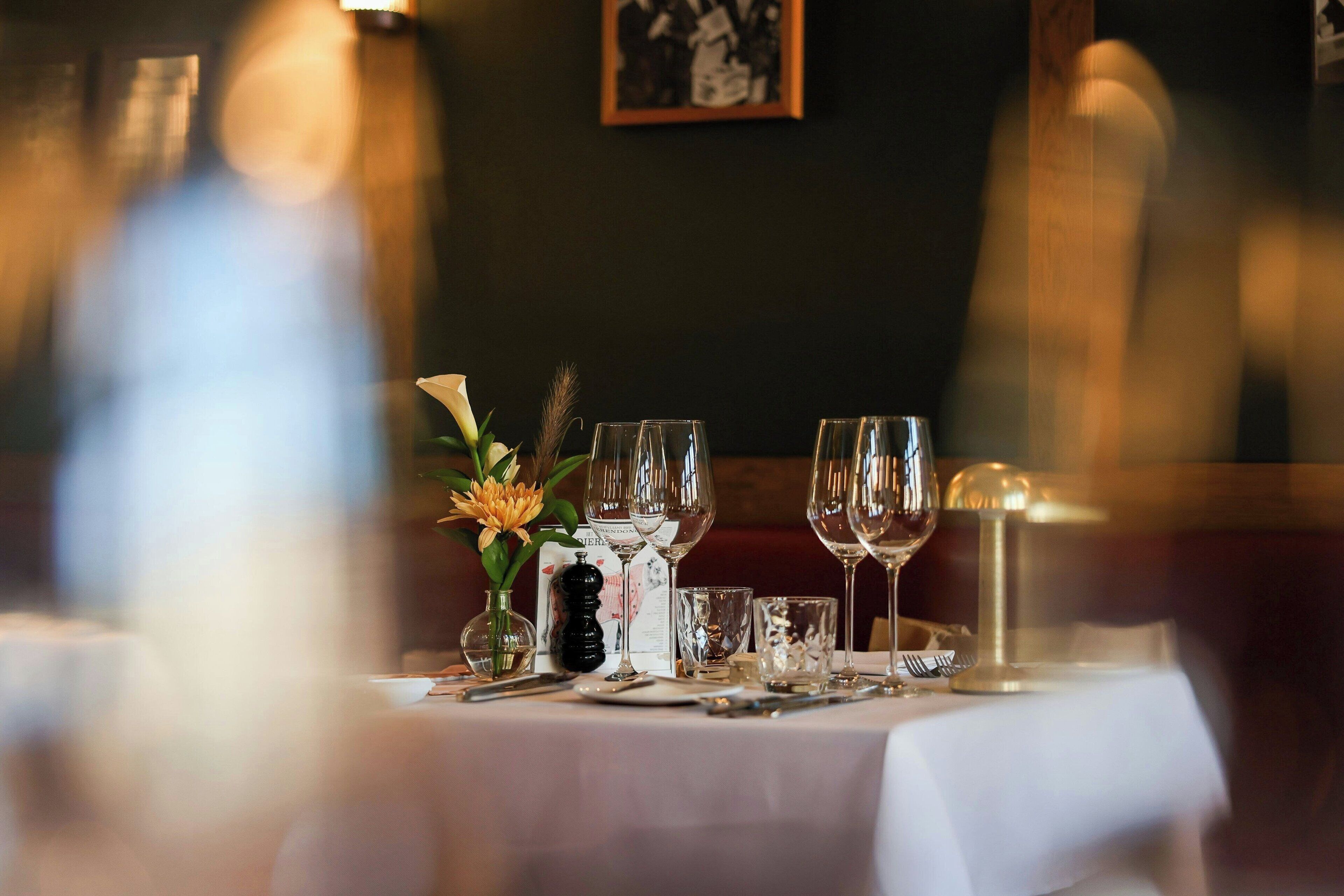 Et spisebord dækket med vinglas, en vase med blomster og en menu.
