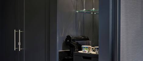 Una cocina moderna con una cafetera, una taza y una copa de vino sobre un estante de vidrio.