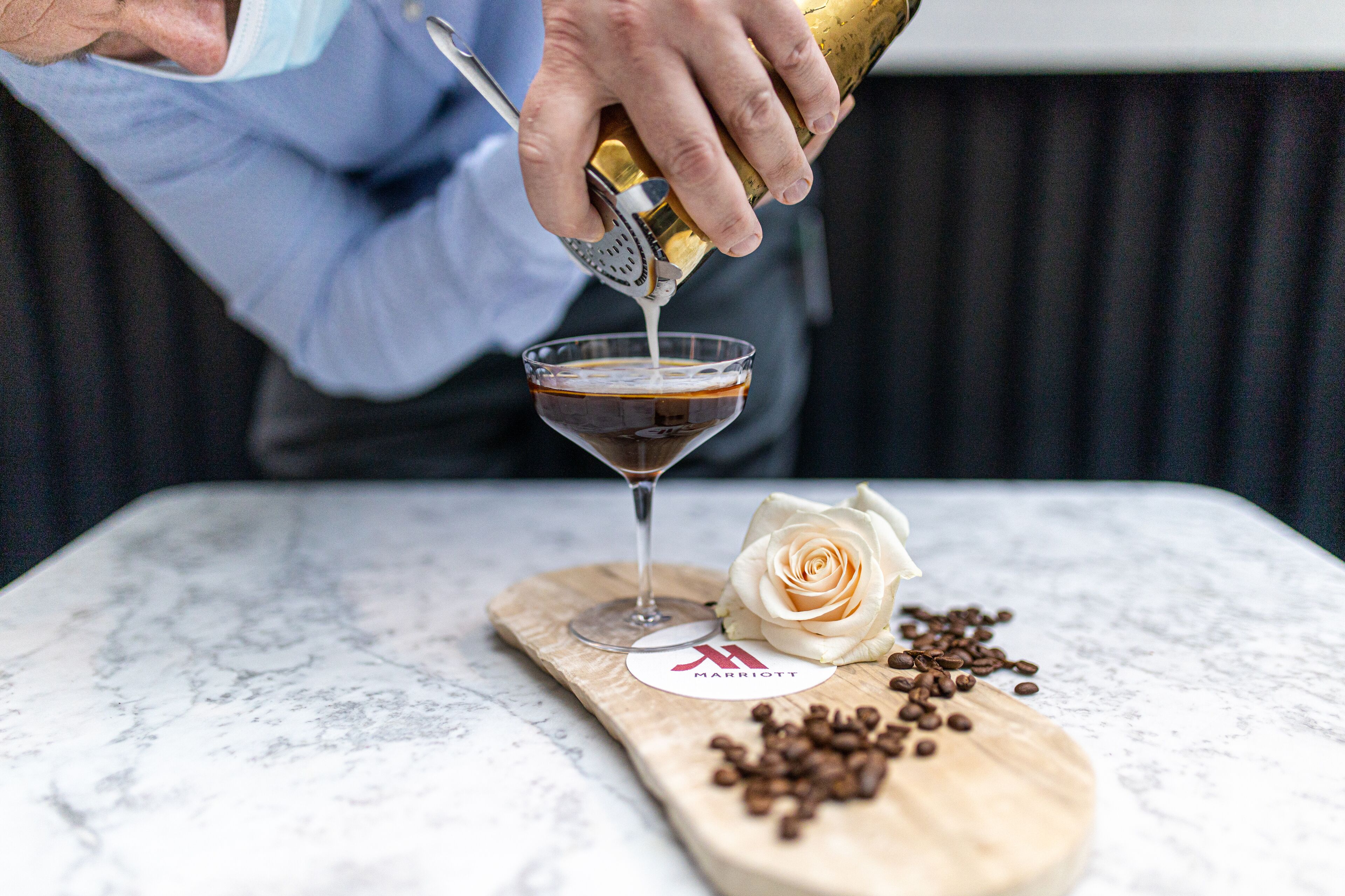 A person pouring a drink into a martini glass on a marble countertop.