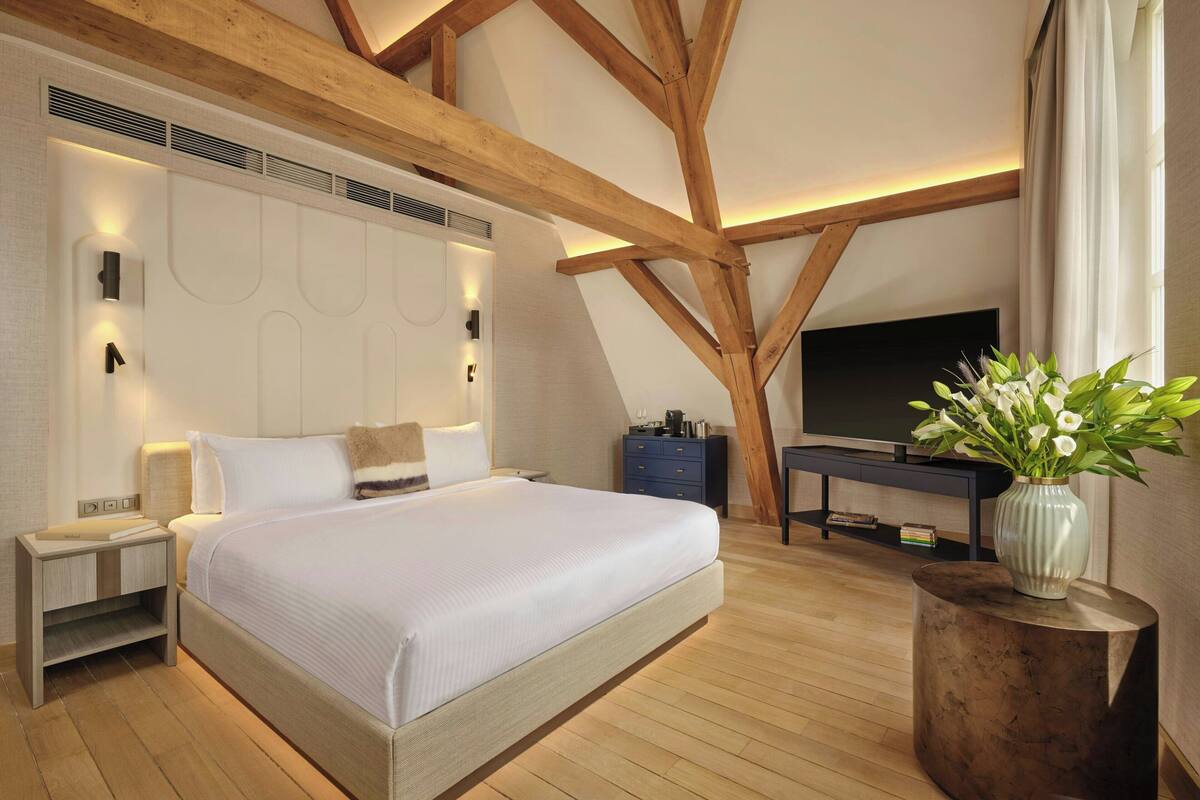 Un dormitorio con una cama grande, mesitas de noche, un televisor y un florero con flores.
