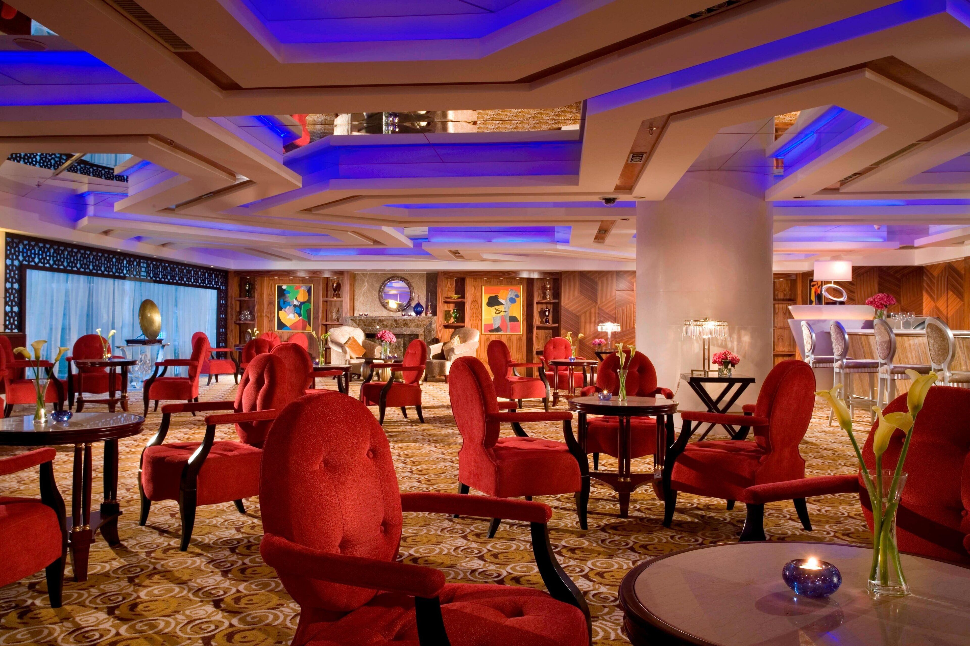A hotel lobby with red upholstered chairs, round tables, and a patterned carpet.