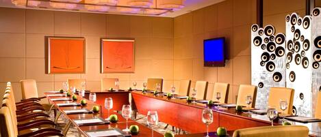 A conference room with long tables, chairs, and a television screen.