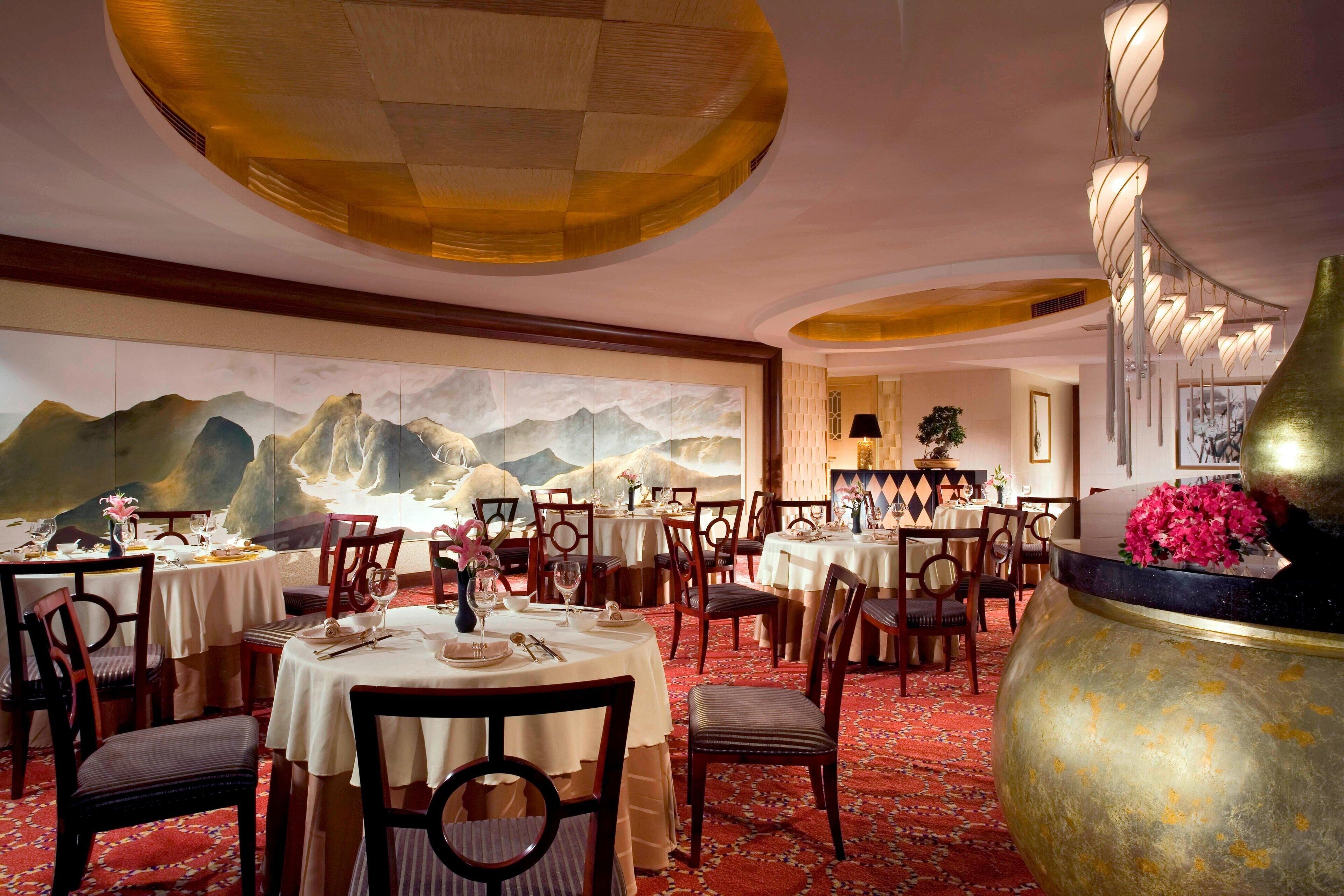 A dining area with round tables, chairs, and a large vase with flowers.