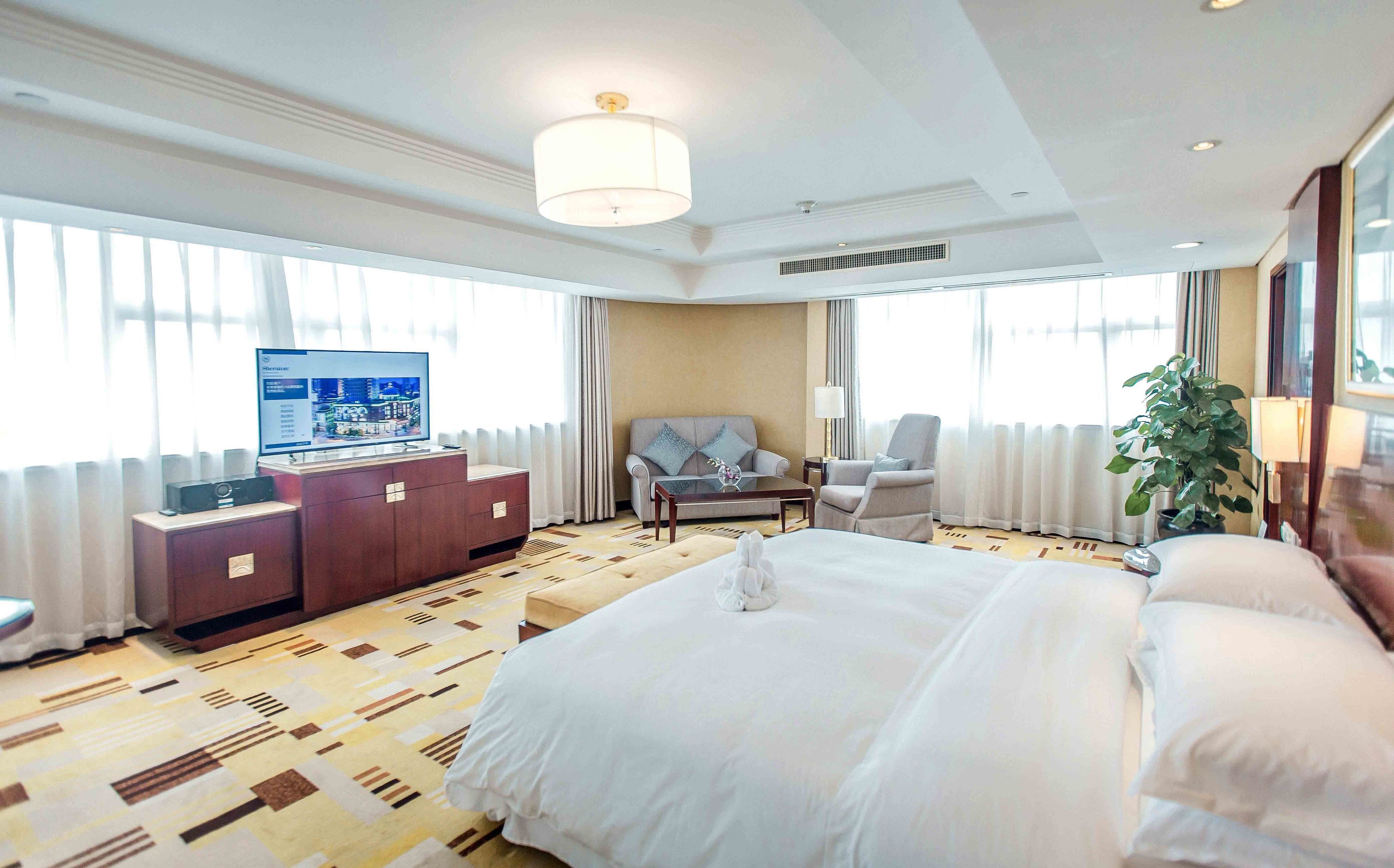 A hotel room with a large bed, a sofa, a desk with a computer, and a TV.