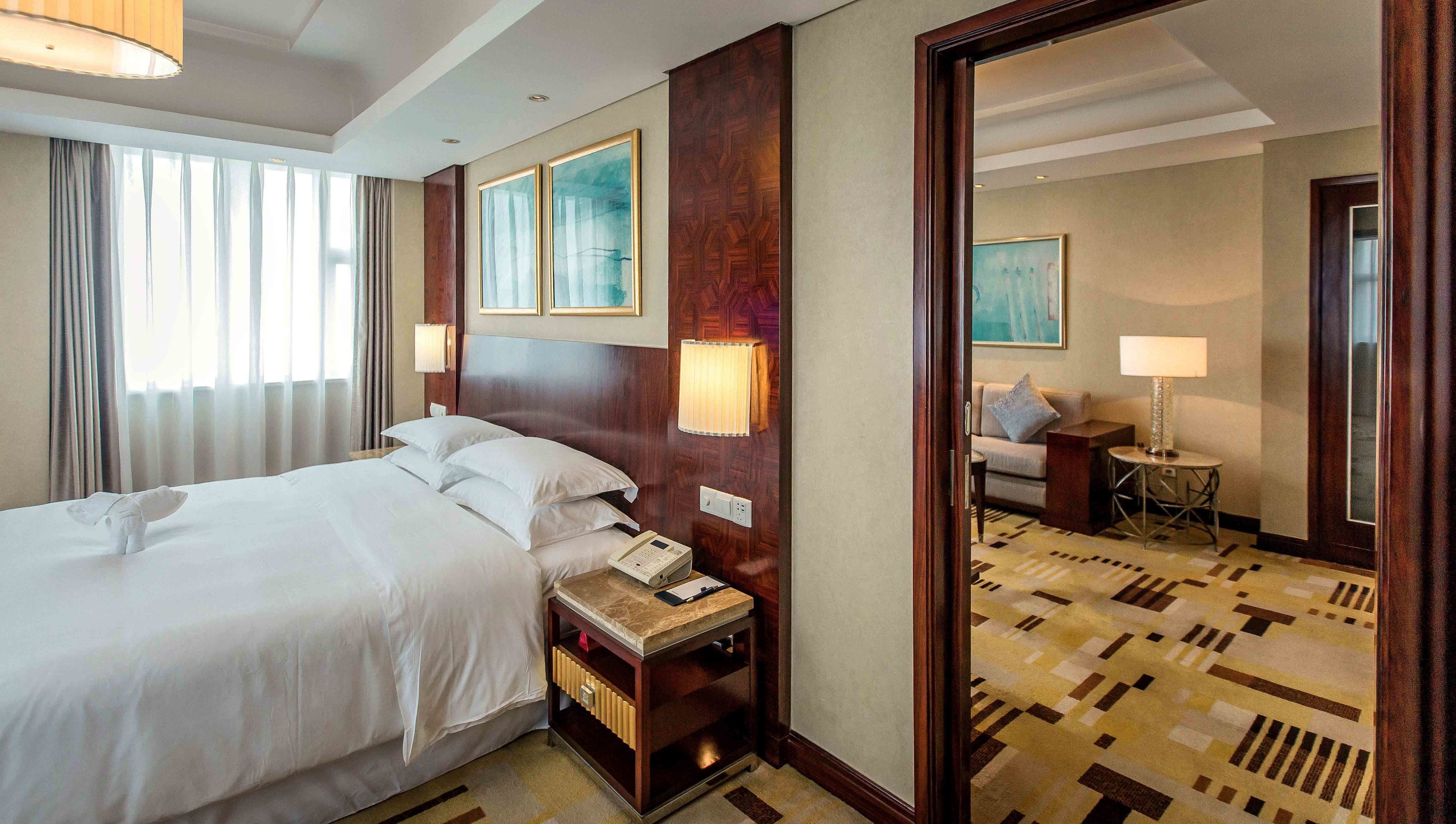 A hotel room with a large bed, bedside table with a phone, a mirror, and a view of the hallway.
