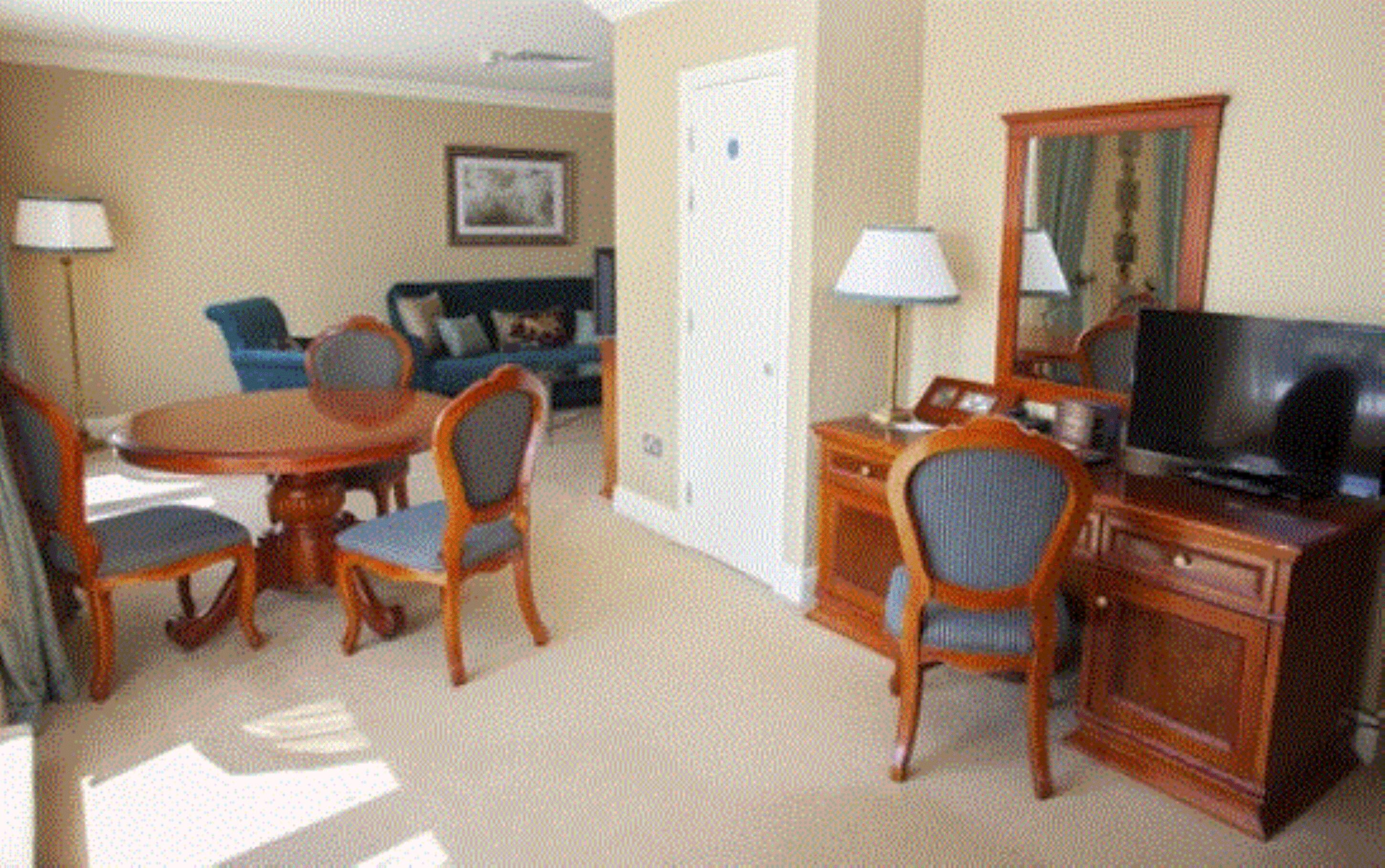 Quarto de hotel com área de refeições, sala de estar com sofá e poltronas, televisão e uma porta.