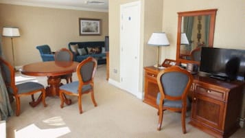 Quarto de hotel com área de refeições, sala de estar com sofá e poltronas, televisão e uma porta.