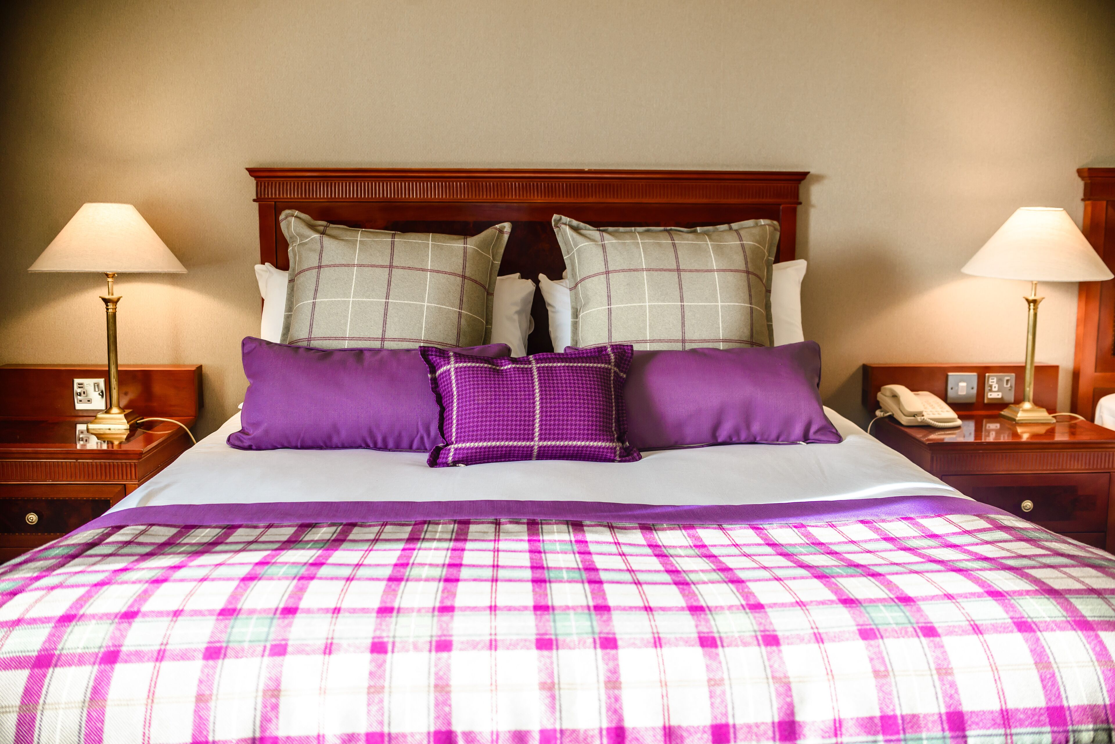 A bed with a plaid bedspread, two nightstands with lamps, and a wooden headboard.