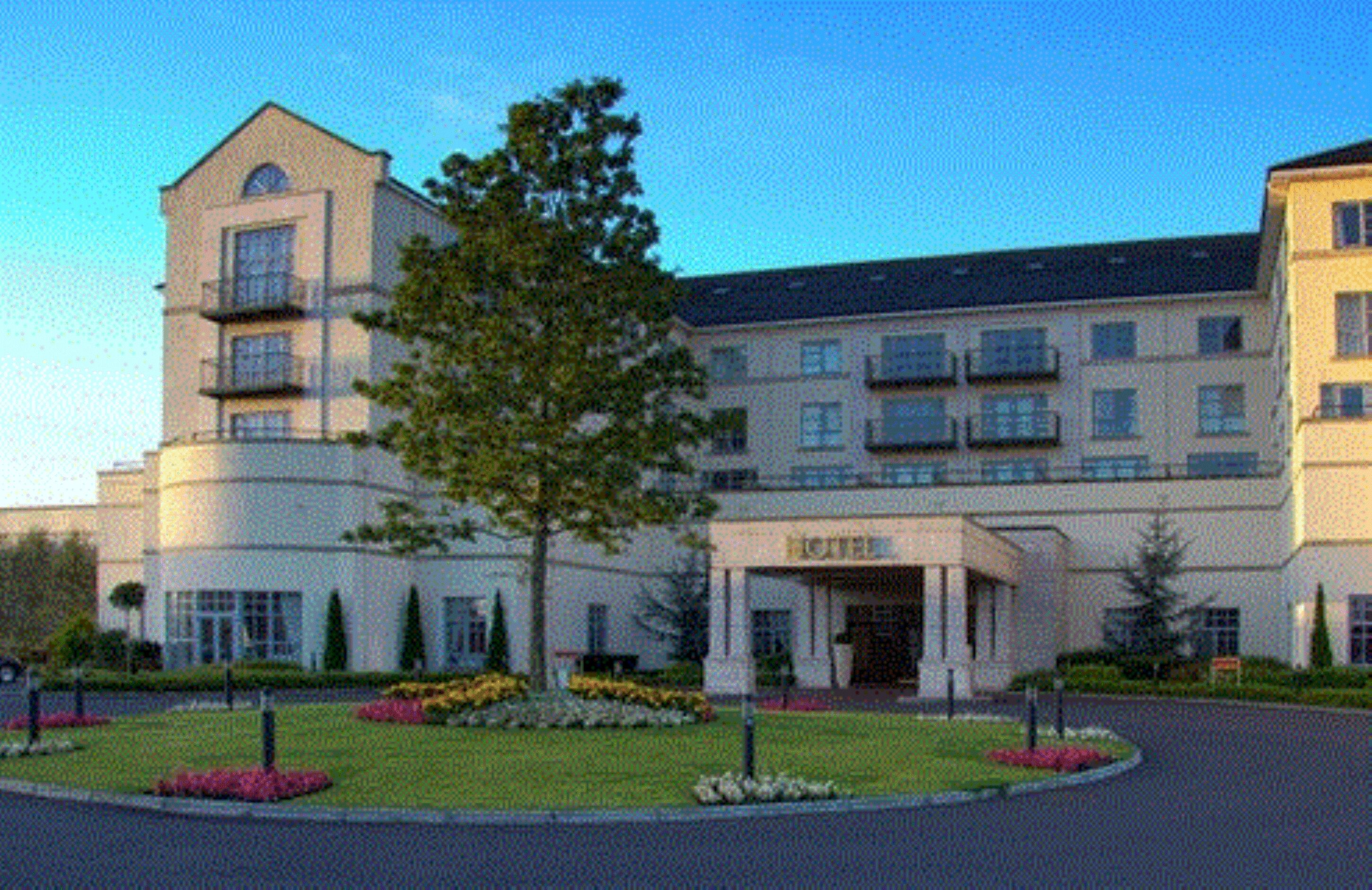 A hotel with a central entrance, multiple floors, and a landscaped garden with trees and flowers.