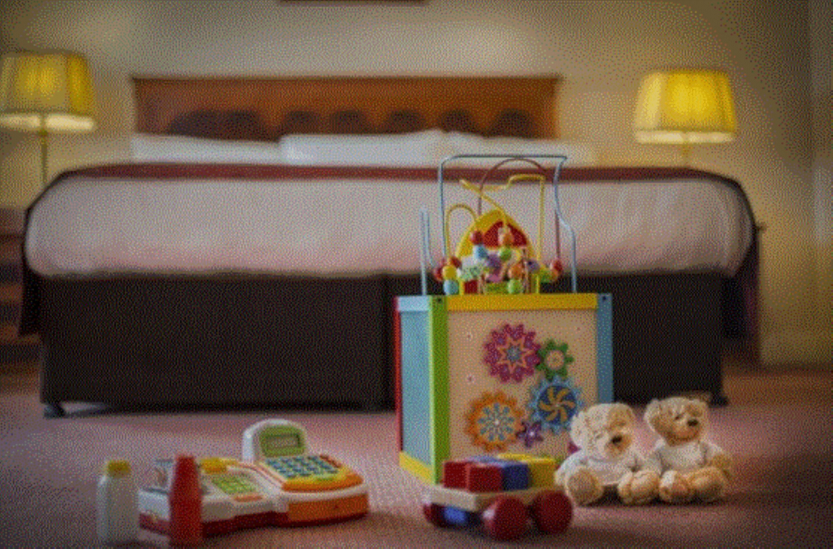 A hotel room with a bed, a toy piano, and two teddy bears on the floor.