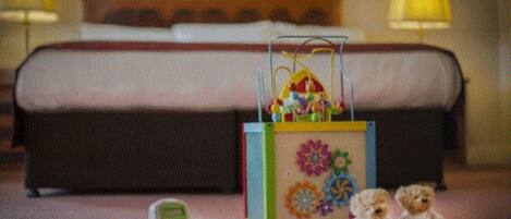 A hotel room with a bed, a toy piano, and two teddy bears on the floor.