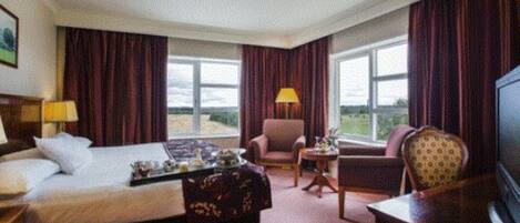 A hotel room with a bed, a desk, a chair, a TV, and large windows.