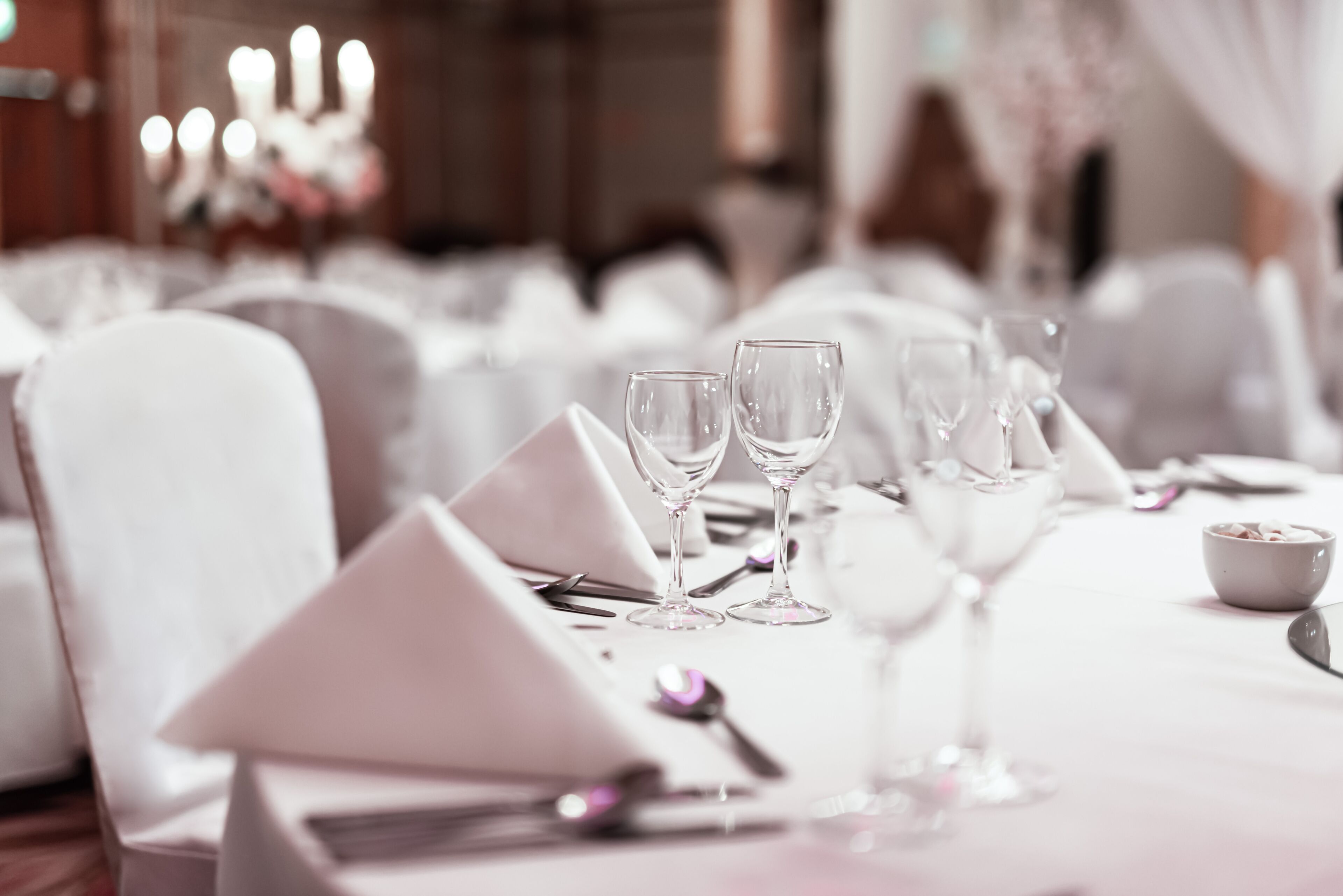 A table set for a formal event with white tablecloths, clear glassware, and neatly arranged cutlery.