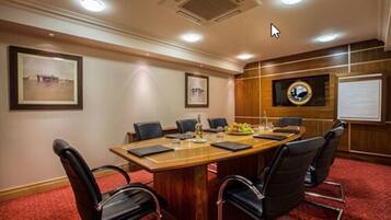 A conference room with a wooden table, black chairs, a whiteboard, and framed pictures on the walls.