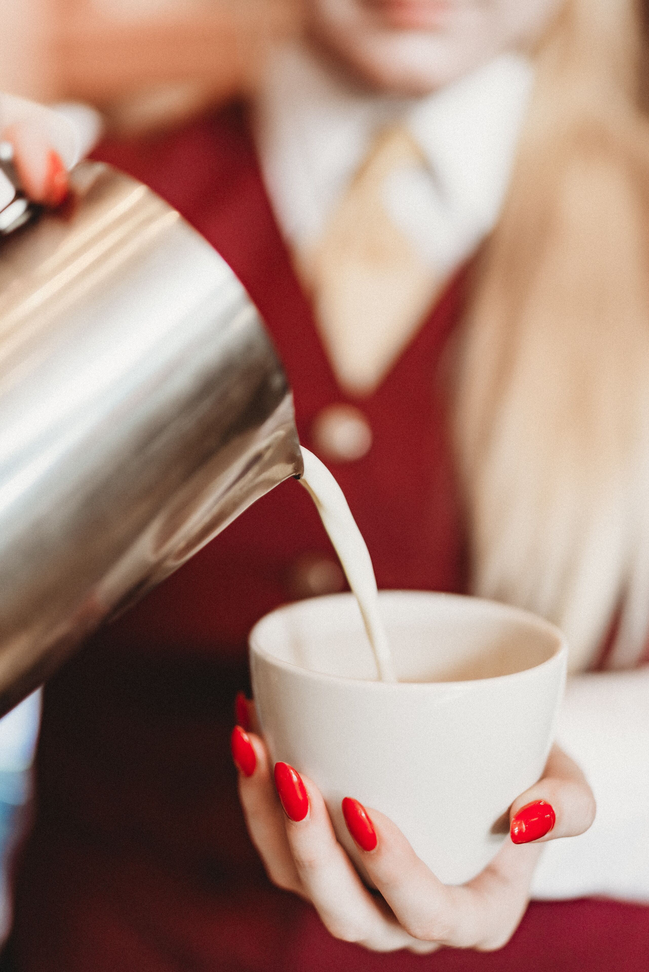 Eine Person gießt Flüssigkeit aus einem Metallbehälter in eine weiße Tasse.