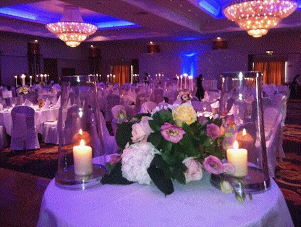 Un salón de banquetes con mesas redondas, centros de mesa florales y velas.