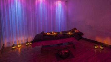 A dimly lit room with a bed, candles, and a massage table.