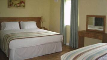 A hotel room with a large bed, a bedside table, a dresser, and a mirror.