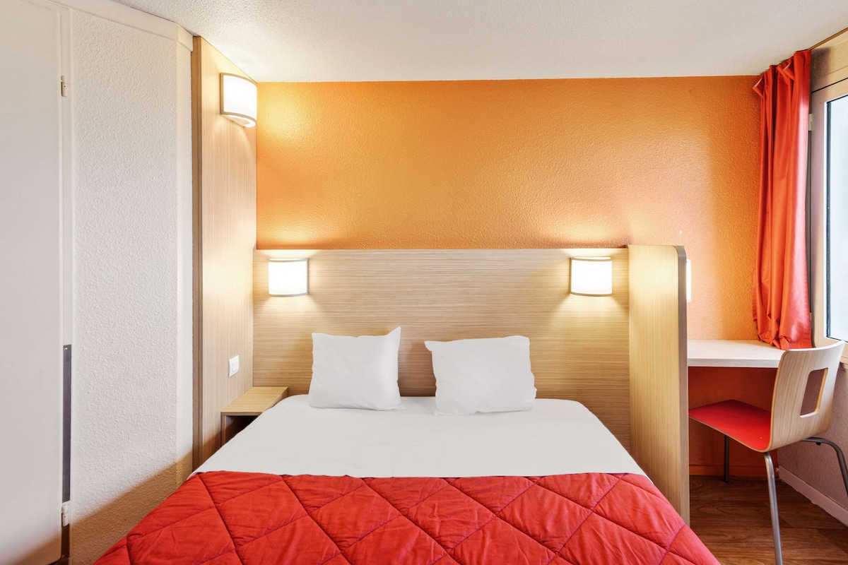 Una habitación de hotel con una cama, dos lámparas de noche, un escritorio y una silla.