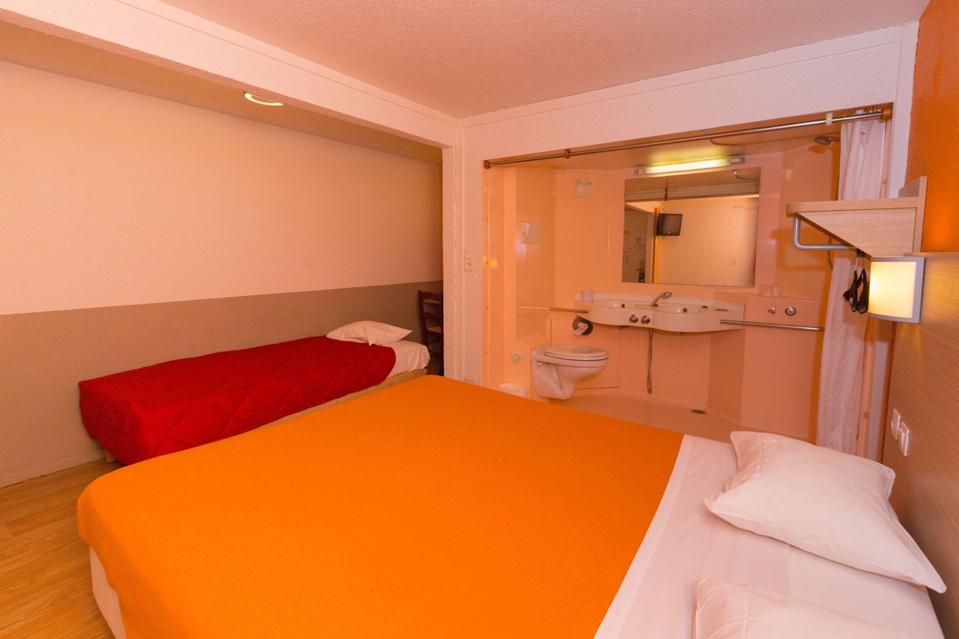 A hotel room with a large bed, a smaller bed, a bathroom with a mirror, and a shower.