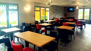 Un restaurant avec plusieurs tables et chaises, un mur en pierre et un écran de télévision.