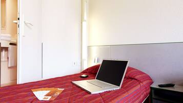 A hotel room with a bed, a laptop, a remote control, and a door to the bathroom.