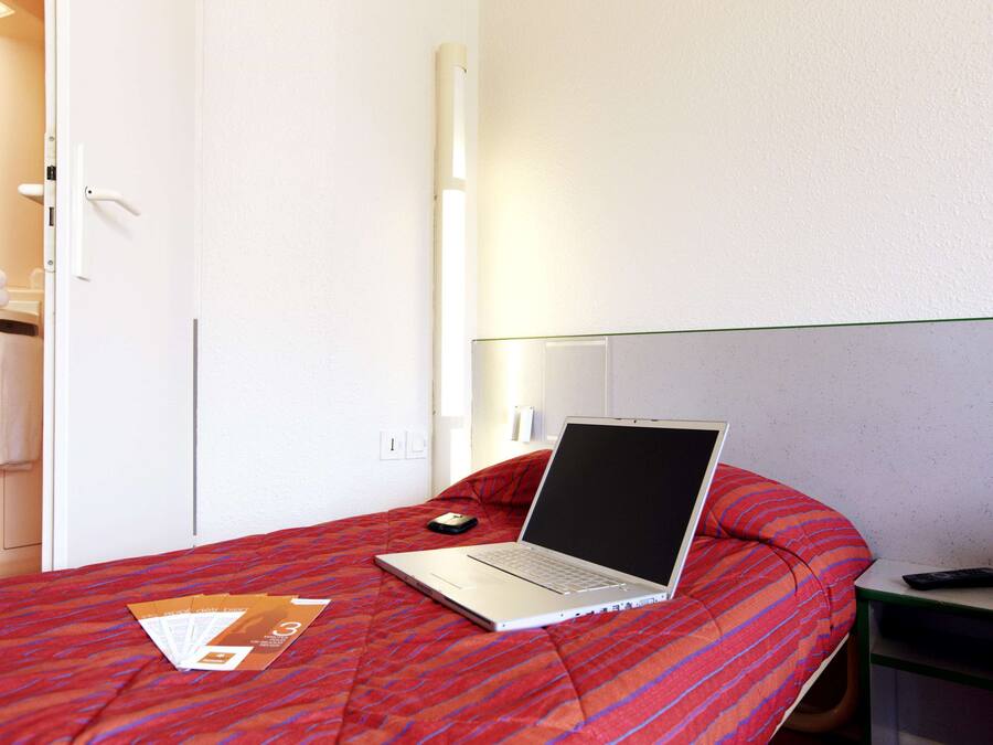 A hotel room with a bed, a laptop, a remote control, and a door to the bathroom.