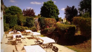 Un espace extérieur aménagé avec des tables et des chaises, entouré de verdure et d’arbres.
