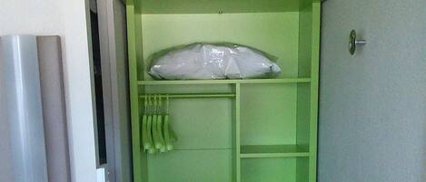 A small, green room with a bed, a pillow, a shelf with toiletries, and a vent on the wall.