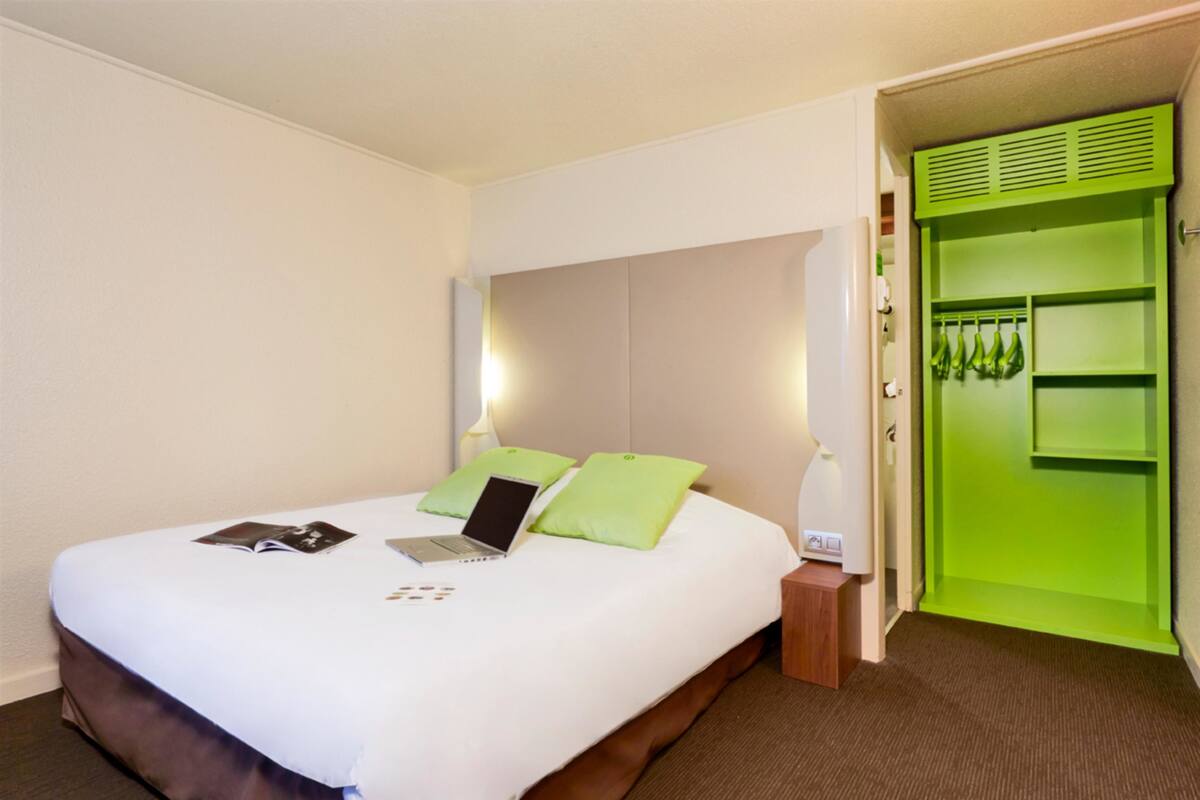 Una habitaci ón de hotel con una cama, una computadora portátil y un armario verde.