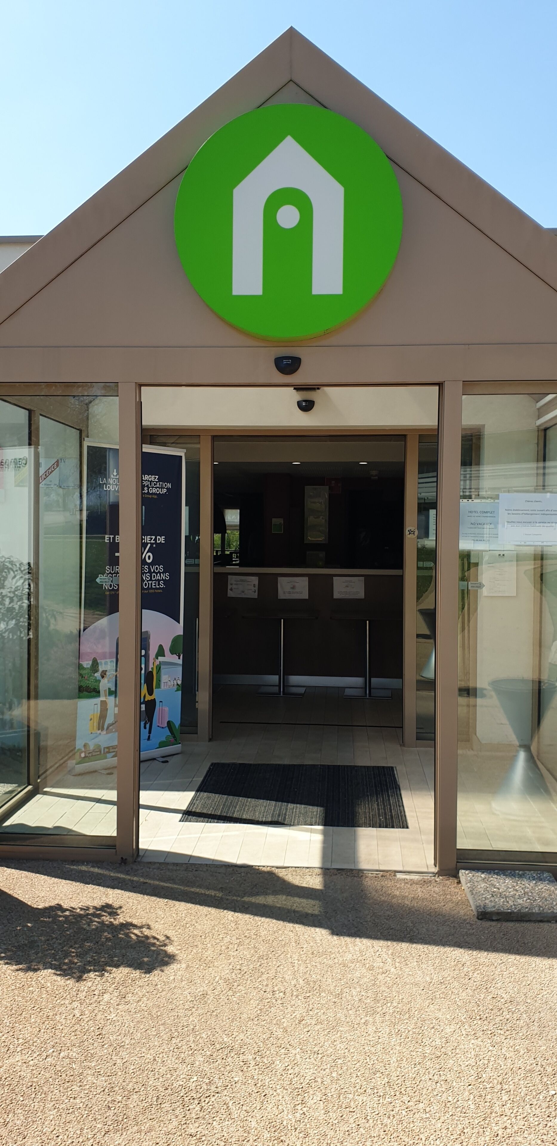 L’entrée d’un hôtel, avec un logo vert, un comptoir d’accueil et un panneau indiquant une réduction de 10 %.