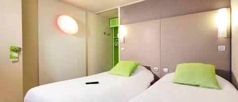 Camera d'hotel con due letti, ciascuno con un cuscino verde, un telecomando sul letto a sinistra e un lampadario fissato al muro.