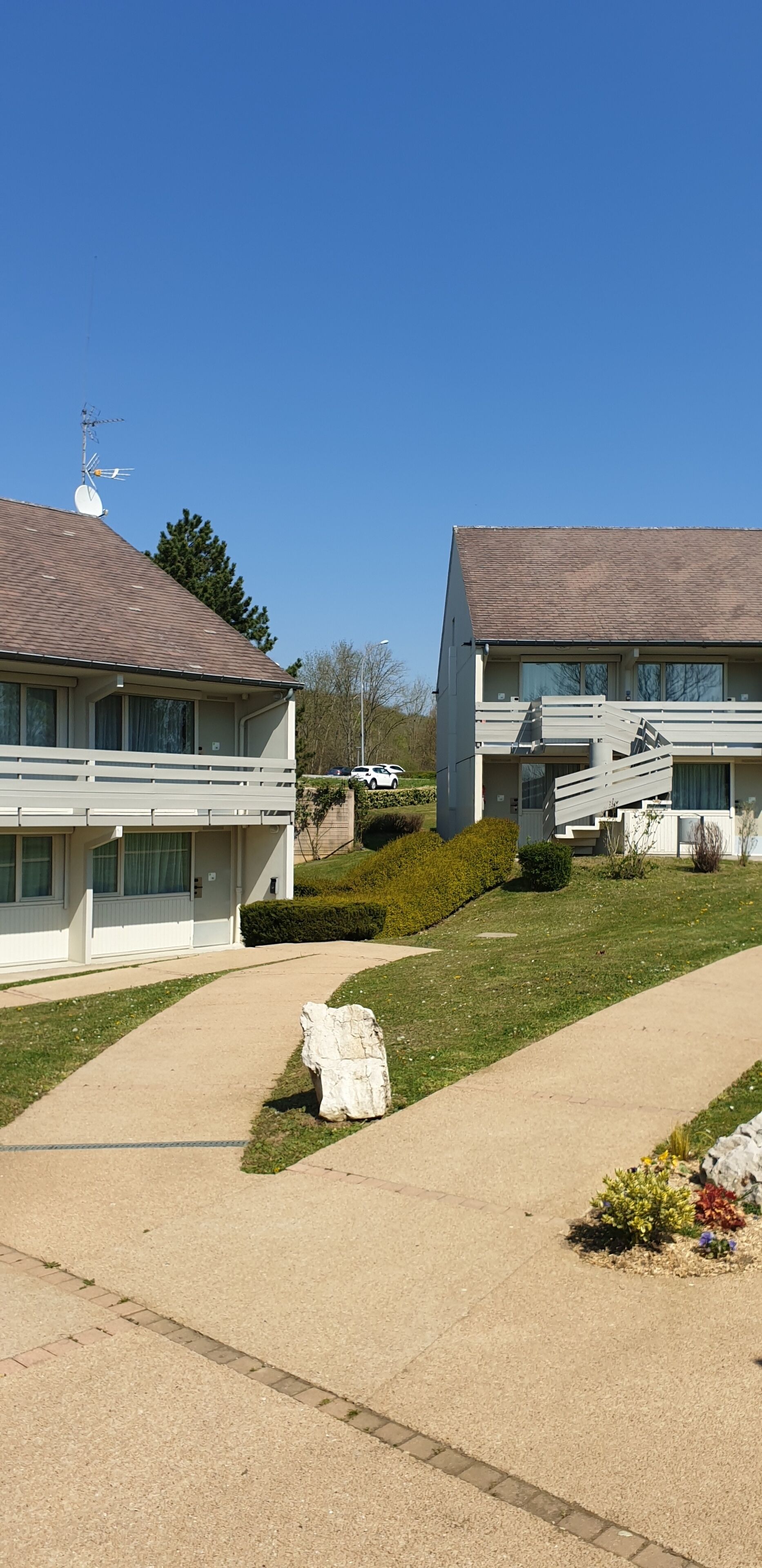 A residential area with two modern houses, a clear sky, and a well-maintained lawn.