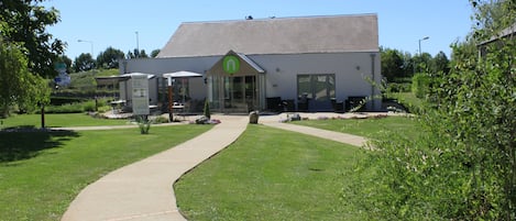 A building with a green logo, a curved pathway leading to the entrance, and a well-maintained lawn.