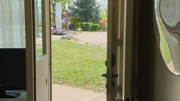 An open door leading to a covered outdoor area with a view of a garden and a building in the distance.