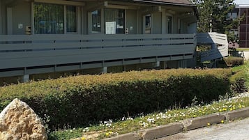 Un edificio con tetto piatto e ampie finestre, circondato da un siepe e un'area con ghiaia.