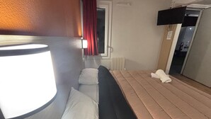 Una stanza con un letto, una finestra con tende rosse, un termosifone e una TV a muro.