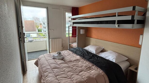 Una camera compatta con un letto a castello, un letto singolo con copripiumino rosa, pavimento in legno e una porta scorrevole in vetro che dà su un balcone.