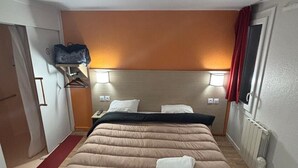 Una camera d'albergo con un letto, due lampade ai comodini, una tenda rossa e un pavimento in legno.