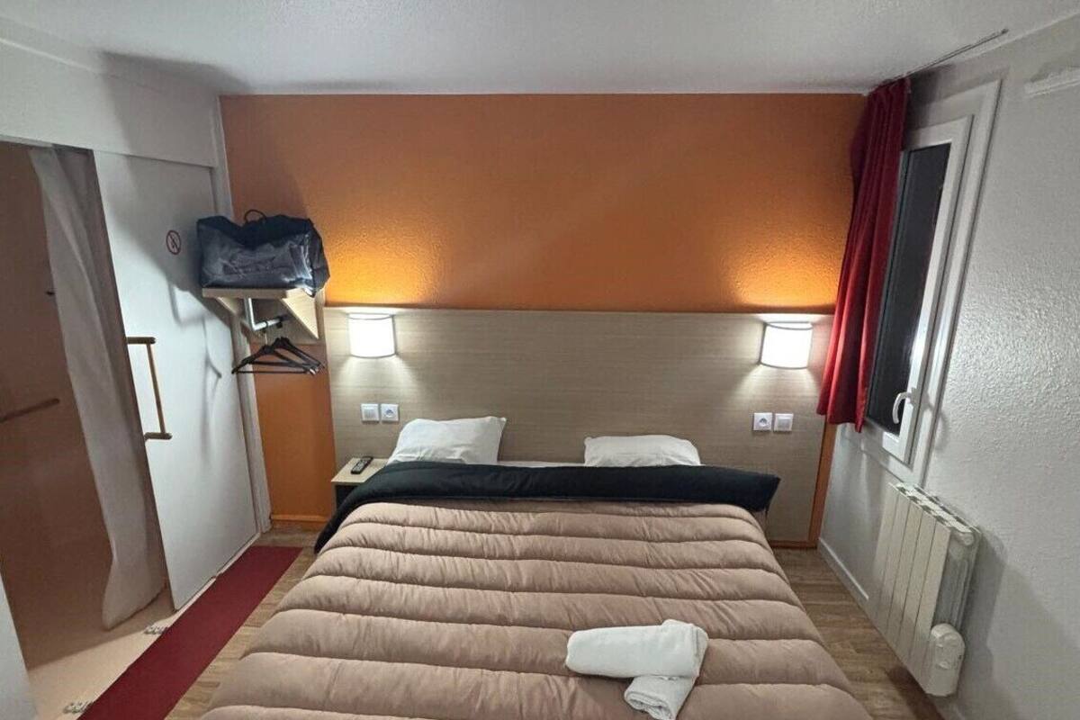 A hotel room with a bed, bedside lamps, a red curtain, and a wooden floor.