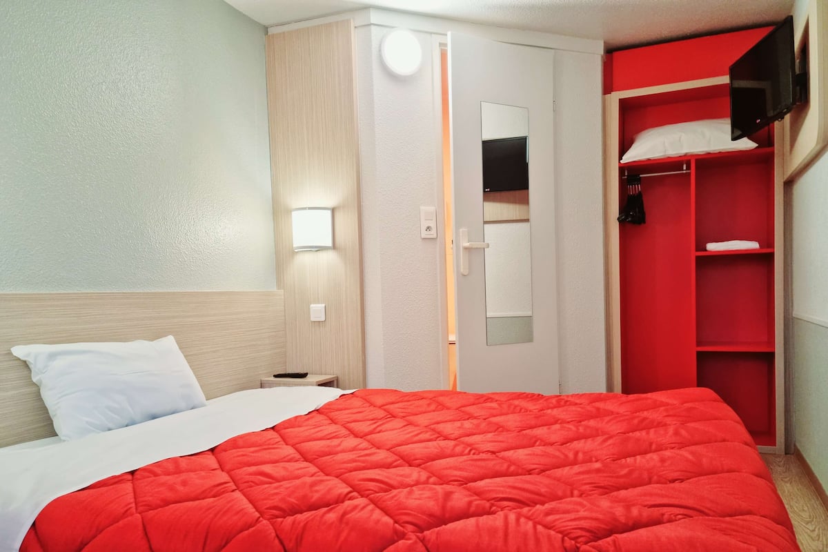 Quarto de hotel com cama, guarda-roupa e espelho.
