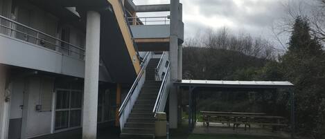 Un edificio de varios niveles con escalera, zona de estar al aire libre y mesa de picnic cubierta.