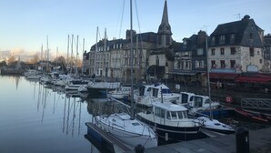 A marina with various boats docked, a prominent church with a spire, and buildings with commercial establishments. - Premiere Classe Honfleur (Honfleur)