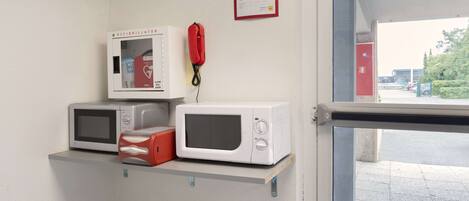 A kitchen area with a microwave and a red telephone on a shelf.