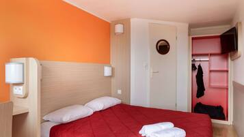 Une chambre d’hôtel avec une couvre-lit rouge, un oreiller blanc, une couverture blanche, un petit miroir rond et un téléviseur fixé au mur.